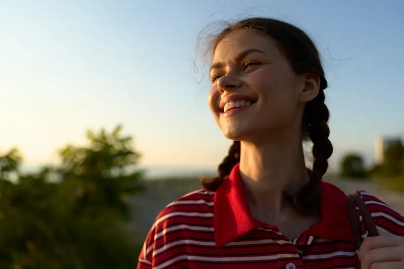 A smiling young woman enjoying lifestyle outdoors at sunset. The happy female looks away with braids in a summer park. Concept for carefree moments, freedom, and joy.