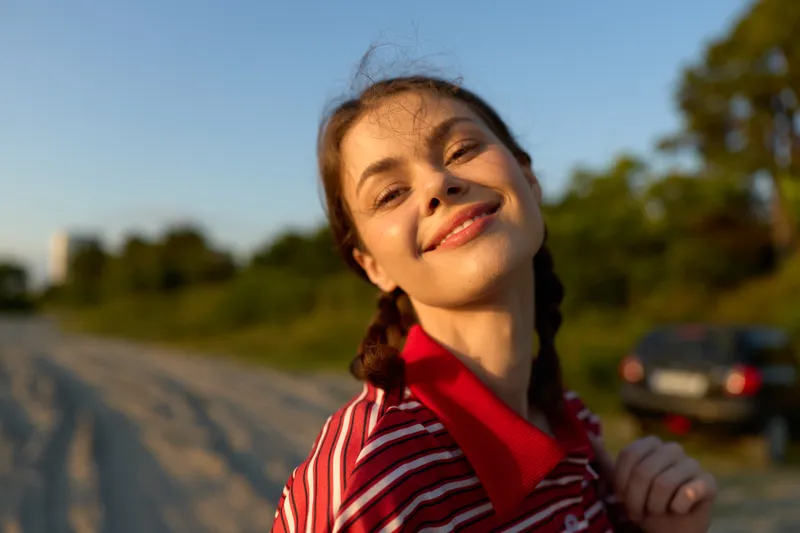 Smiling woman lifestyle portrait outdoor at sunset. Young happy person looking at camera during golden hour light. Concept of freedom, nature, joy, summer, weekend, leisure and authentic mood.