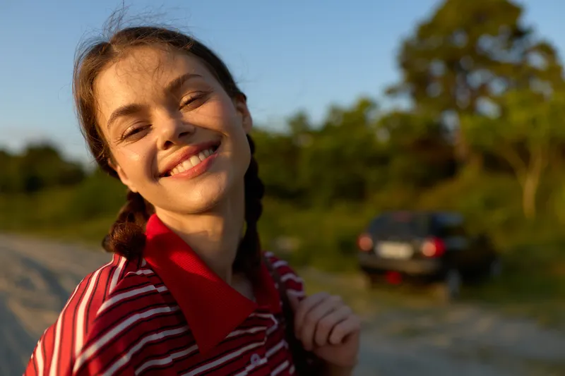 Smiling woman enjoying outdoor lifestyle during sunny day. Portrait of happy girl with braids in summer nature. Concept of freedom, joy, and travel adventure in warm golden light.