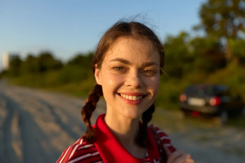 Smiling woman lifestyle portrait outdoor at sunset. The natural face of a girl with braids looks happy. Soft warm golden light during summer evening in the nature, authentic beauty.